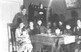 Julafton firas hemma hos familjen Karlsson på Kvarnfallet 31, 1930-tal. Från vänster Alma Karlsson med sonen Rolf i knät, Viktor Karlsson, barn samt släkt runt ett bord i vardagsrummet.