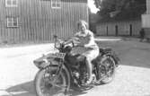 Astrid Karlsson (gift Garthman) grenslar en MC, Indian 1000cc, med sidovagn. Troligtvis är det pojkvännen Helmer Garthmans. Kvarnfallet 31, år 1936.