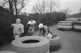 Fyra barn leker utomhus bland stora traktordäck som ligger två och två på varandra vid Katrinebergs daghem. Ett utav barnen sitter på marken, innanför två däck. I bakgrunden finns flera däck som ligger två och två.