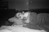 Ett dagisbarn, liggandes på sidan, sover på en utlagd madrass på golvet. Vid sidan om står ett glas vatten. Barnet har en filt på sig. Katrinebergs daghem 1992.