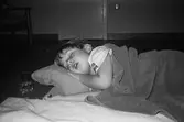 Ett dagisbarn, liggandes på sidan, sover på en utlagd madrass på golvet. Vid sidan om står ett glas vatten. Barnet har en filt på sig. Katrinebergs daghem 1992.