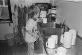 Flickan Alexandra står vid diskbänken. Hon häller upp vatten i en vit kaffemugg, ifrån en rinnande kran. Lunkentussen, Katrinebergs daghem, 1992.