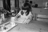 Cecilia sitter vid ett bord och färglägger med hjälp av färgpennor, förtryckta figurer på ett A4-blad. Flickan är mycket koncentrerad. Lunkentussen, Katrinebergs daghem 1992.