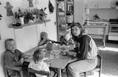 Linda Olausson och fyra barn sitter vid ett lågt bord och äter. På bordet finns använda tallrikar, glas, bestick och en plastbägare. Linda håller på med att skära upp en banan på ett fat. Hoppetossan, Katrinebergs daghem 1992.