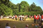 Ett folkdanslag, uppklädda i dräkter, dansar inför beskådare i Gunnebo slottspark.