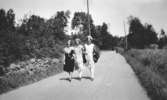 Tre unga kvinnor promenerar på en landsväg. Karin Hasselberg (längst till vänster), en väninna och systern Valborg Hasselberg. 1920- till 30-tal.