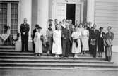 En grupp människor står på Gunnebo slottstrappa, 1930-tal. Hilda Sparre står i vit klänning i mitten och håller en herre under armen.