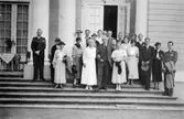 En grupp människor står på Gunnebo slottstrappa, 1930-tal. Hilda Sparre står i vit klänning i mitten och håller en herre under armen.