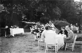 Män och kvinnor sitter kring några bord i Gunnebo slottspark, 1930-tal.