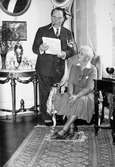 Skådespelaren Anders de Wahl tittar ner i  ett papper, ståendes bredvid Hilda Sparre som sitter i en fåtölj. Gunnebo slott, april 1939.