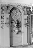 Reliefdekor på Matsalens västra vägg samt porslinsföremål och två vägglampetter med slipade kristallprismor och plats för tre ljus. Gunnebo slott 1930-tal.