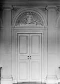 Dubbeldörr, mellan Salongen och Ovala vestibulen, med relief i halvcirkel ovanför. Reliefen föreställer en pokal med skäror och trädgårdsverktyg. Gunnebo slott 1930-tal.
