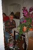 Ove Höglund sitter vid ett bord som är fullt med blommor. Detta i samband med avtackningen av Johan och Anna-Greta Ryhag. De hade deltagit som frivilligarbetare i utgrävningarna på Gunnebo slott under ledning av arkeolog Lou Schmitt. November 1995.