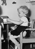 En flicka sitter vid ett bord och har ett set med kopp och fat framför sig. Holtermanska daghemmet 1953.