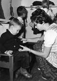En lärarinna hjälper ett barn med kläder. Holtermanska daghemmet 1953.