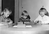 Tre barn som ritar vid ett bord. Holtermanska daghemmet 1953.