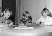 Tre barn som ritar vid ett bord. Holtermanska daghemmet 1953.