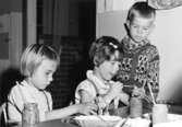 Tre barn som pysslar vid ett bord. Holtermanska daghemmet 1953.