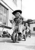 Två pojkar som cyklar på trehjulingar varav den främre är klädd i cowboy-kläder. Holtermanska daghemmet juni 1974.