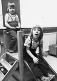 Två barn i en liten rutschbana inomhus. Holtermanska daghemmet maj 1975.