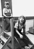 Två barn i en liten rutschbana inomhus. Holtermanska daghemmet maj 1975.