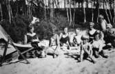 Barn och kvinnor sitter på en sandstrand, troligtvis vid Tulebosjön, 1930-tal.