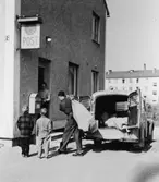 Chaufför Gustav Jarneving ute på dagens första filial-, bunt- och
expresskörning. Här bärs posten in vid postexpeditionen Eskilstuna 5.
I dörren står stationsmästaren Karin Andersson.