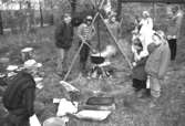 Familjesöndag vid Börjesgården, 1994-05-15. Besökare ser på när Museichef Mari-Louise Olsson kokar soppa över öppen eld. Längst ner till vänster ses museitekniker Alf Garthman.