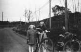 Systrarna Karin (gift Hansson) och Eva (gift Kempe) Pettersson är på cykeltur med sina föräldrar vid Lindomebyvägen (Kyrkängen i Lindome), år 1952.
Eva som är äldst, har fått en ny cykel.