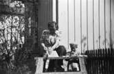 En lärare och ett barn sågar någonting i trädgården vid

Krokslätts daghem, Dalhemsgatan 7 i Krokslätt år 1949.