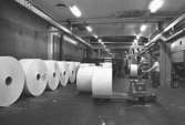 En arbetare kör truck med en pappersbal och ställer den tillsammans med andra pappersbalar.
Bilden ingår i serie från produktion och interiör på pappersindustrin Papyrus, 1980-tal.