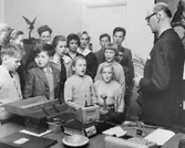 Genom högtalaranläggningen på intendent Carlssons tjänsterum fick
barnen sjunga sin egen sparvisa för postsparbankens personal. T.h.
dirigenten och läraren. komminister Landin.