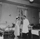 Avdelningsläkare Dr. Bjorwill och assisterande sköterska går rond på Sabbatsbergs sjukhus i Stockholm, cirka 1958. Det låg 20 st patienter i varje sal, 10 st på var sida.