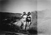 Två bikiniklädda kvinnor lutar sig mot en bergsknalle och solar, troligtvis vid Tulebosjön cirka 1930. Höger sida av fotografiet är ljus-skadat.