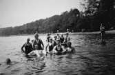 Karl Alberts ligger på rygg i Tulebosjön, 1930-tal. I närheten finns barn och vuxna som står/simmar i vattnet.