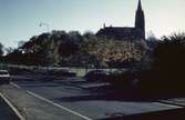 Bilar står parkerade på Häradsgatan i Mölndal, 1970-tal. Fässbergs kyrka tronar i bakgrunden.