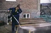 Exteriörfoto från upprustningen av Mölndals Museum år 1985. Museitekniker Sven-Olof Svensson högtryckssprutar några brädor.
