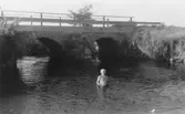 Sommar i Lindome i början av 1940-talet. En kvinna badar i vattnet (troligtvis Lindomeån). I bakgrunden ses en stenbro. Samma plats som 2007_0459.