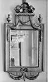 Vägghängd, avlång träspegel med dekor. I spegelglaset ses delar av ett rum samt med kristallkrona. Gunnebo slott 1930-tal.