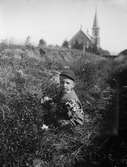 Ivar Liljefors plockar blommor på ängen med Mikaelskyrkan i bakgrunden, Uppsala 1900 - 1901