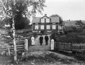 Tre oidentifierade individer framför hus på landet.