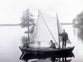 Tre män i en segelbåt på en spegelblank sjö. En av personerna på bilden är Gunnar Håkansson.