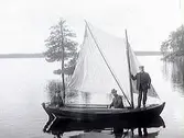Tre män i en segelbåt på en spegelblank sjö. En av personerna på bilden är Gunnar Håkansson.