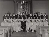 Kyrkoherde Rosén (i mitten) med komfirmandgrupp framför altartavlan i Tvååkers kyrka, år 1939. 
Flickorna i ljusa klänningar och pojkarna mörka kostymer.