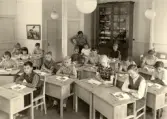 Eleverna sitter i sina skolbänkar under Magister Andersson vakande öga i Alltorps skola, 1940-tal