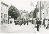 Konstapel Evert Petersson ledsagar en musikkår (hemvärnets?) uppför Norrgatan vid Hantverkets dag, 5/7 1942.
I bakgrunden skymtar Norrtullskolan.