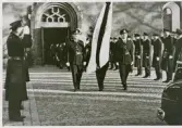 Poliskommissarie Sture Sandells (1912-1964) begravning i Växjö domkyrka, oktober 1964.
Begravningsföljet lämnar kyrkan, med paraderande poliser på båda sidor.
Notera de toppknäckta granarna på var sida om kyrkporten, enligt gammal tradition.