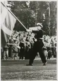 Poliskonstapel Olle Strömkvist paraderar med svenska flaggan vid Svenska Flaggans dag (6 juni) 1958 på Värendsvallen,
Växjö.
