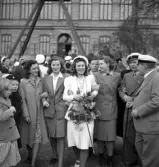 Studentfinal, 1944. 
En kvinnlig student med uppvaktning, på skolgården till  Växjö Högre 
Allmänna Läroverk. 

Angående avgångsklassen 1944 - se 