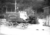 Kraftkarl, ifrån atletklubben Heros, drar Hellkvist bagerivagn med tänderna. På vagnen sitter tre kvinnor och en pojke. Tidigt 1900-tal.